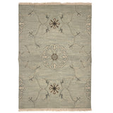 Handwoven rug sample with fringe in a floral filigree pattern in grey, brown and cream on a grey-blue field.