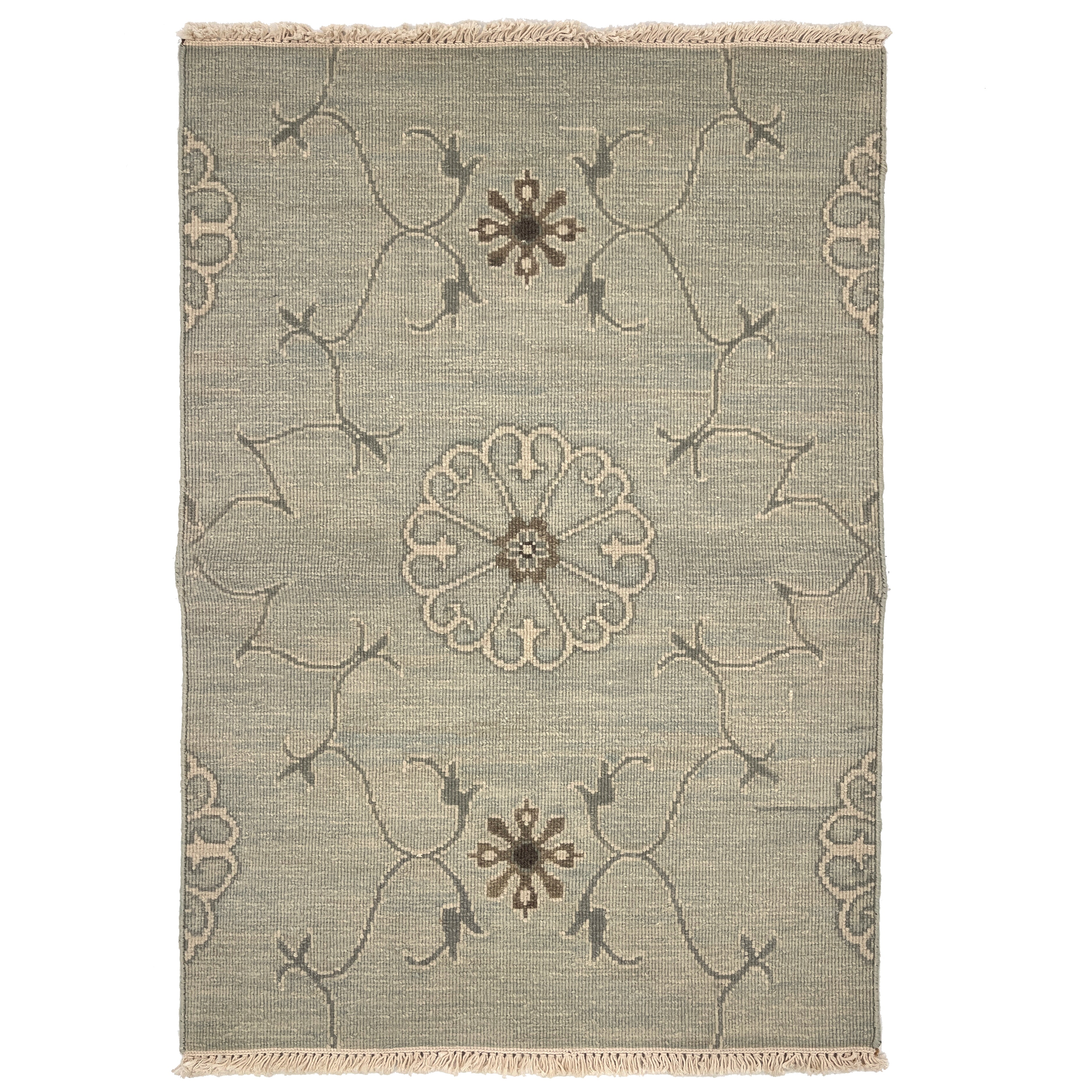 Handwoven rug sample with fringe in a floral filigree pattern in grey, brown and cream on a grey-blue field.