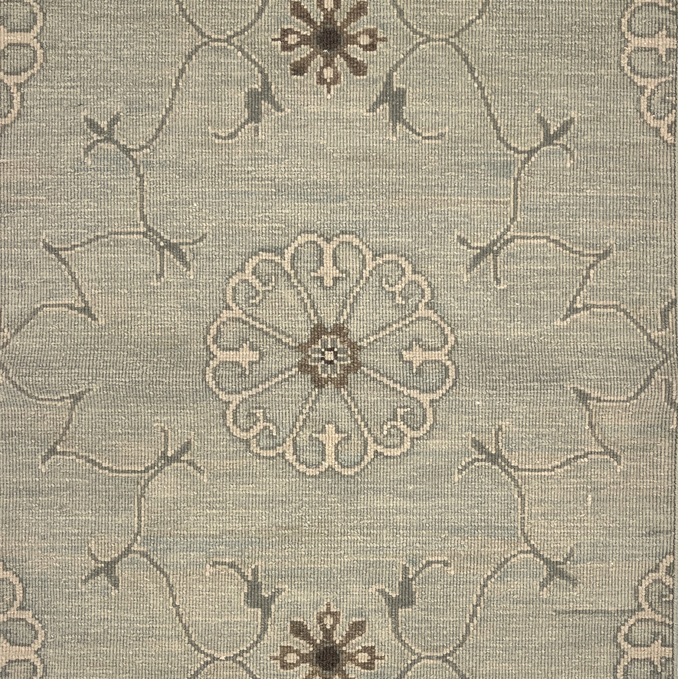 Close up of hand woven rug in a floral filigree pattern in grey, brown and cream on a grey-blue field.