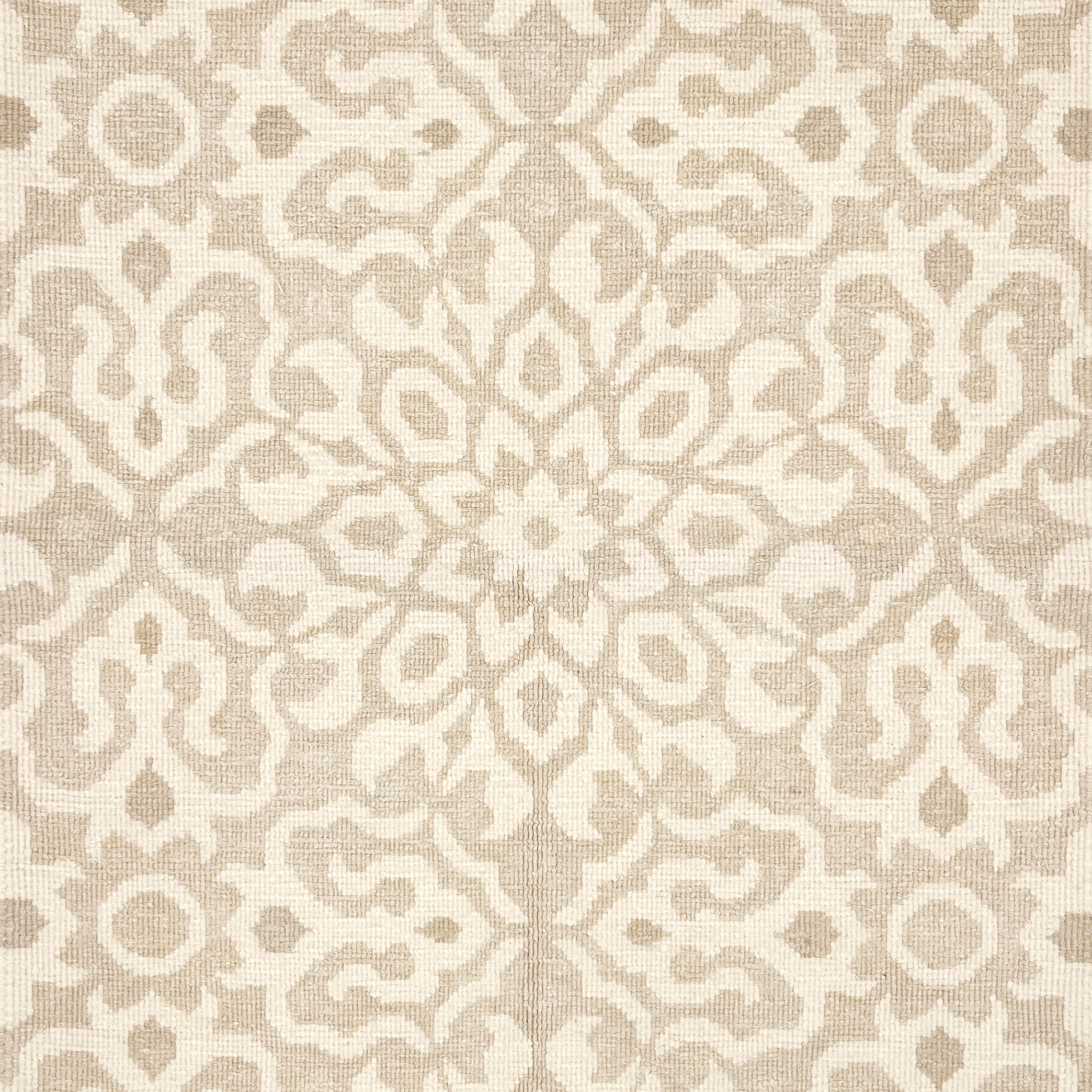 Close up of a handwoven rug in an ornate damask medallion design in cream on a beige field. 