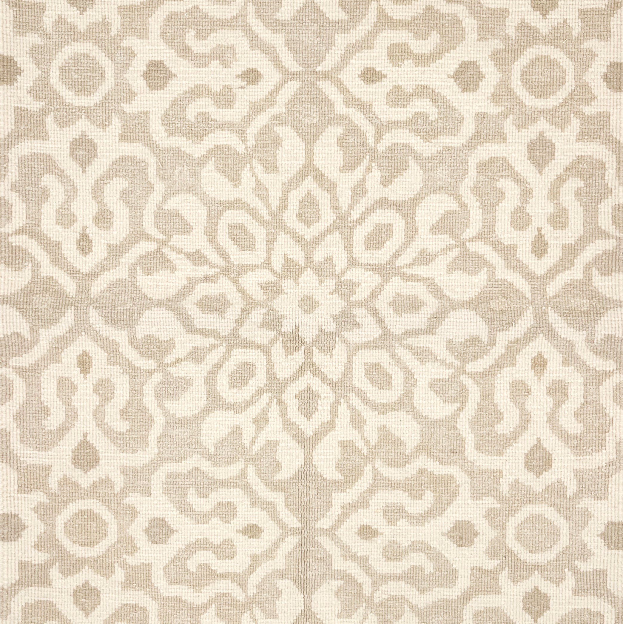 Close up of a handwoven rug in an ornate damask medallion design in cream on a beige field. 