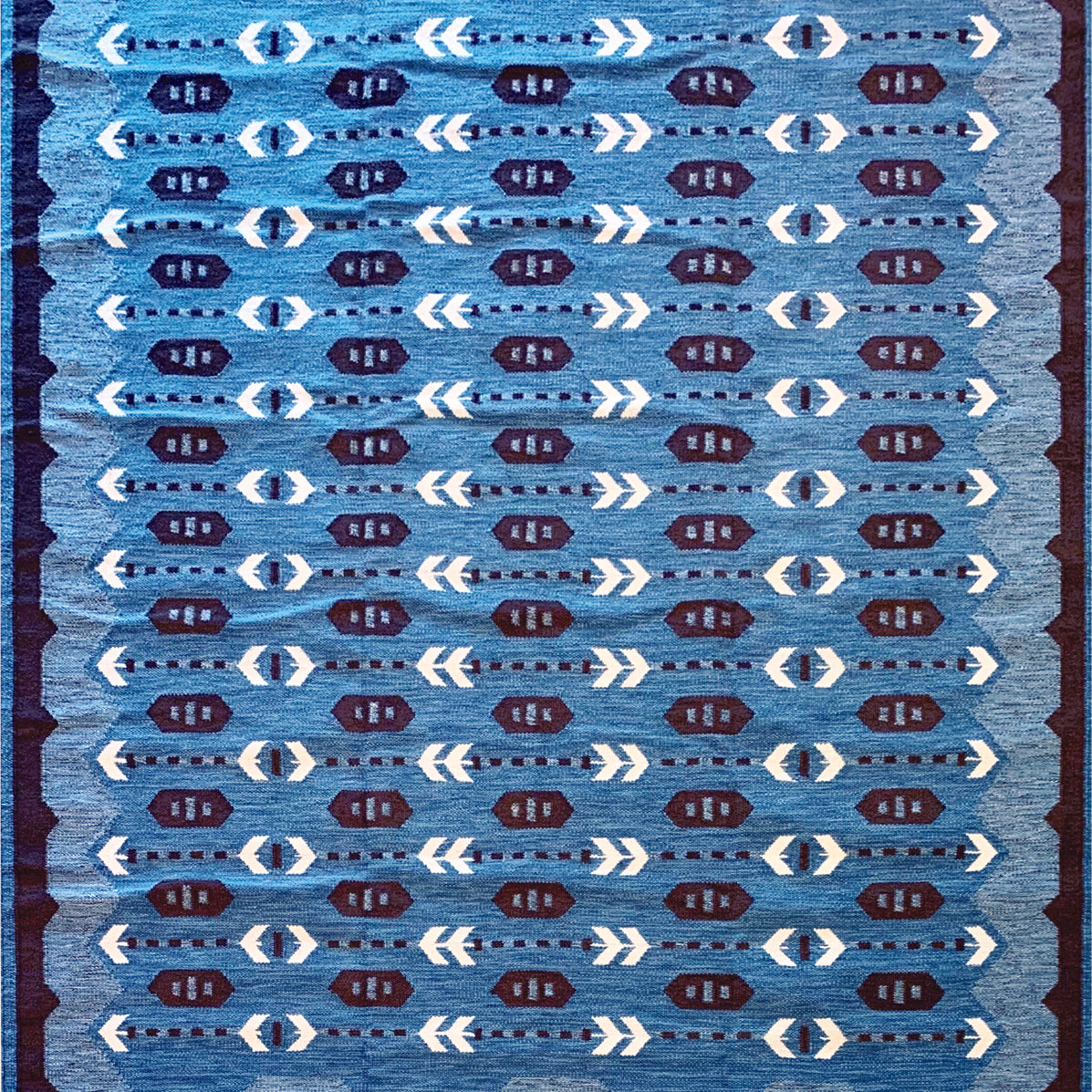 Handwoven rug in a Swedish arrow design in brown and white on a green field. 