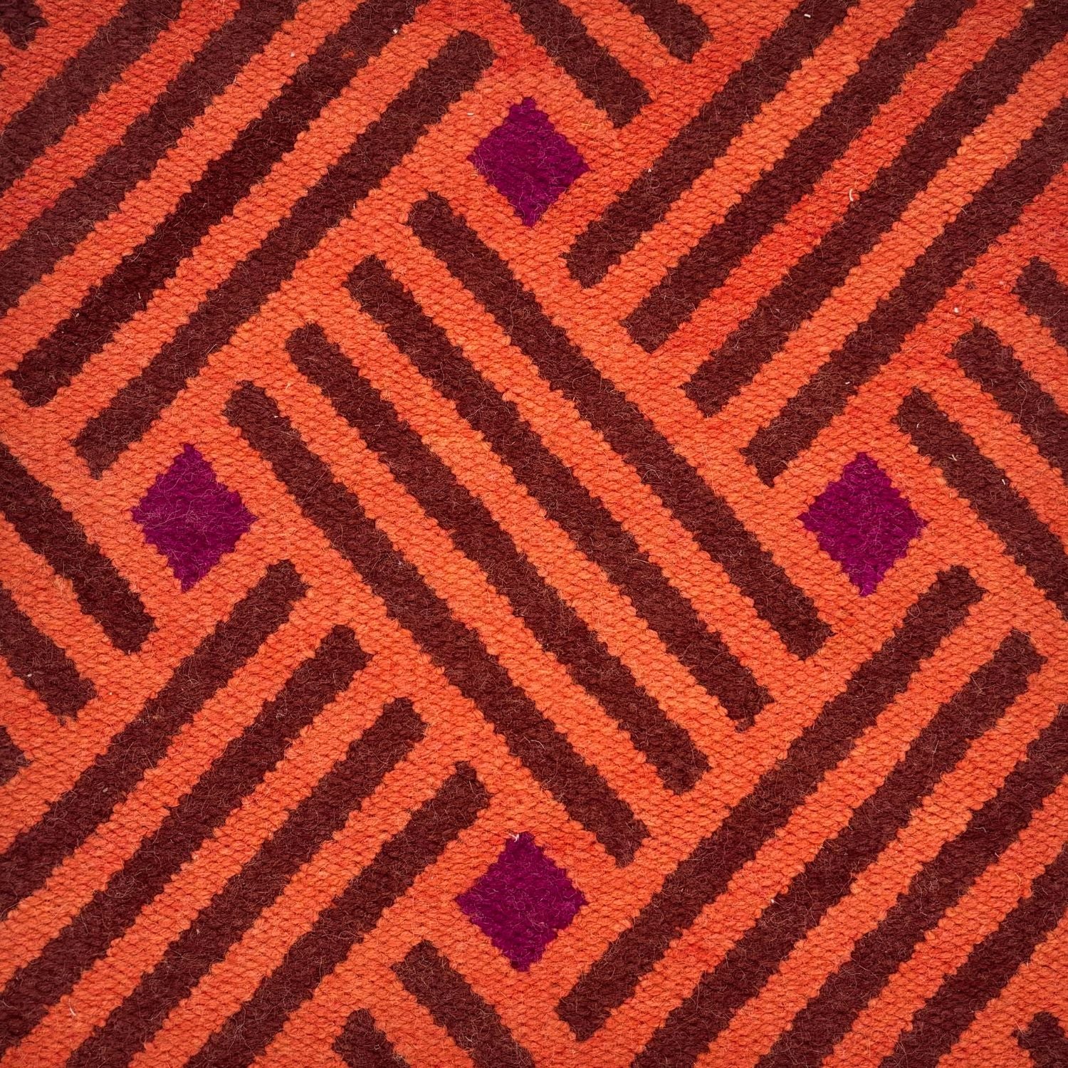 A woven rug with diagonal stipes in orange and brown and diamonds of purple.
