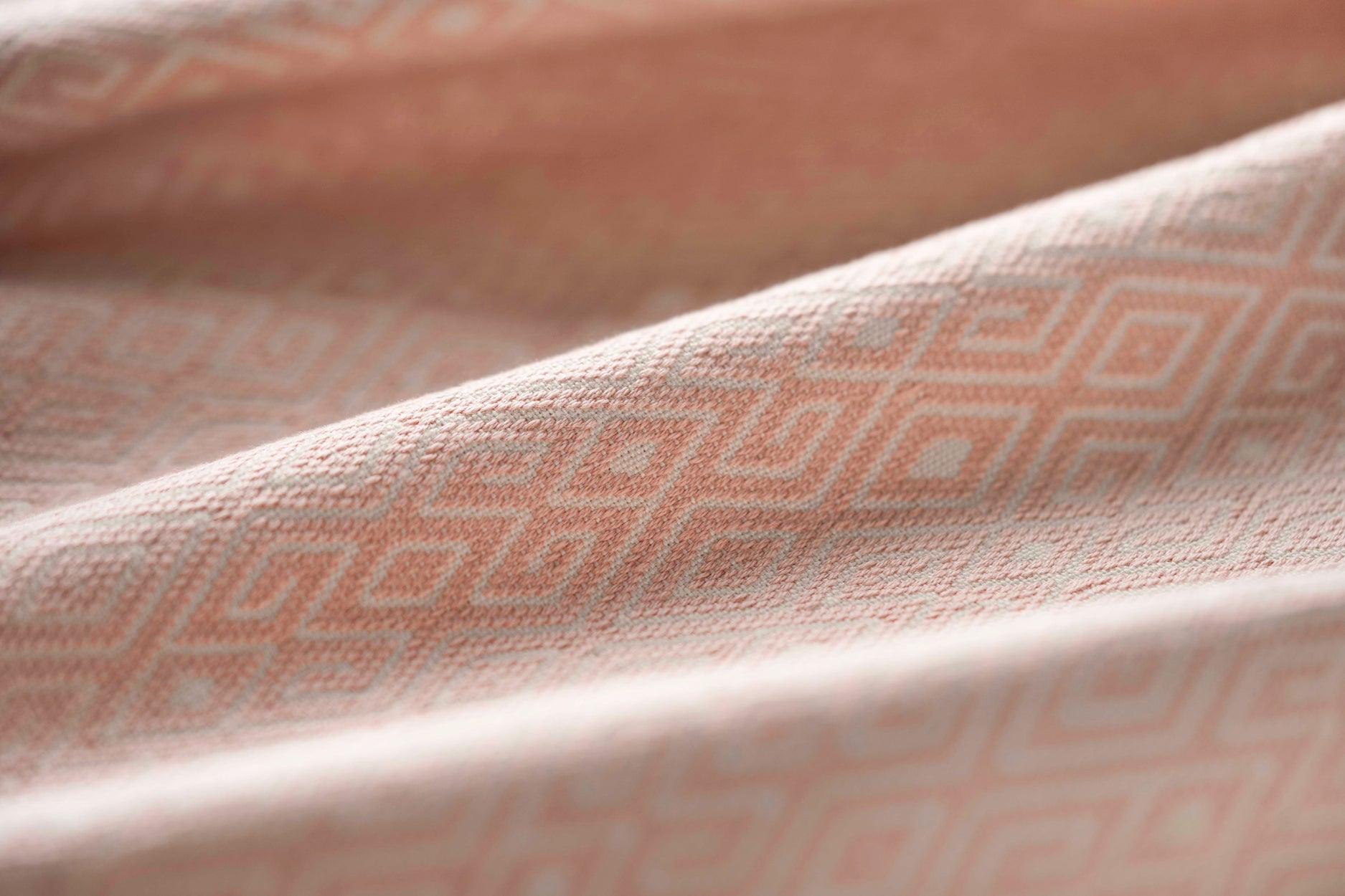 Close-up of light pink fabric with a subtle geometric pattern gently folded