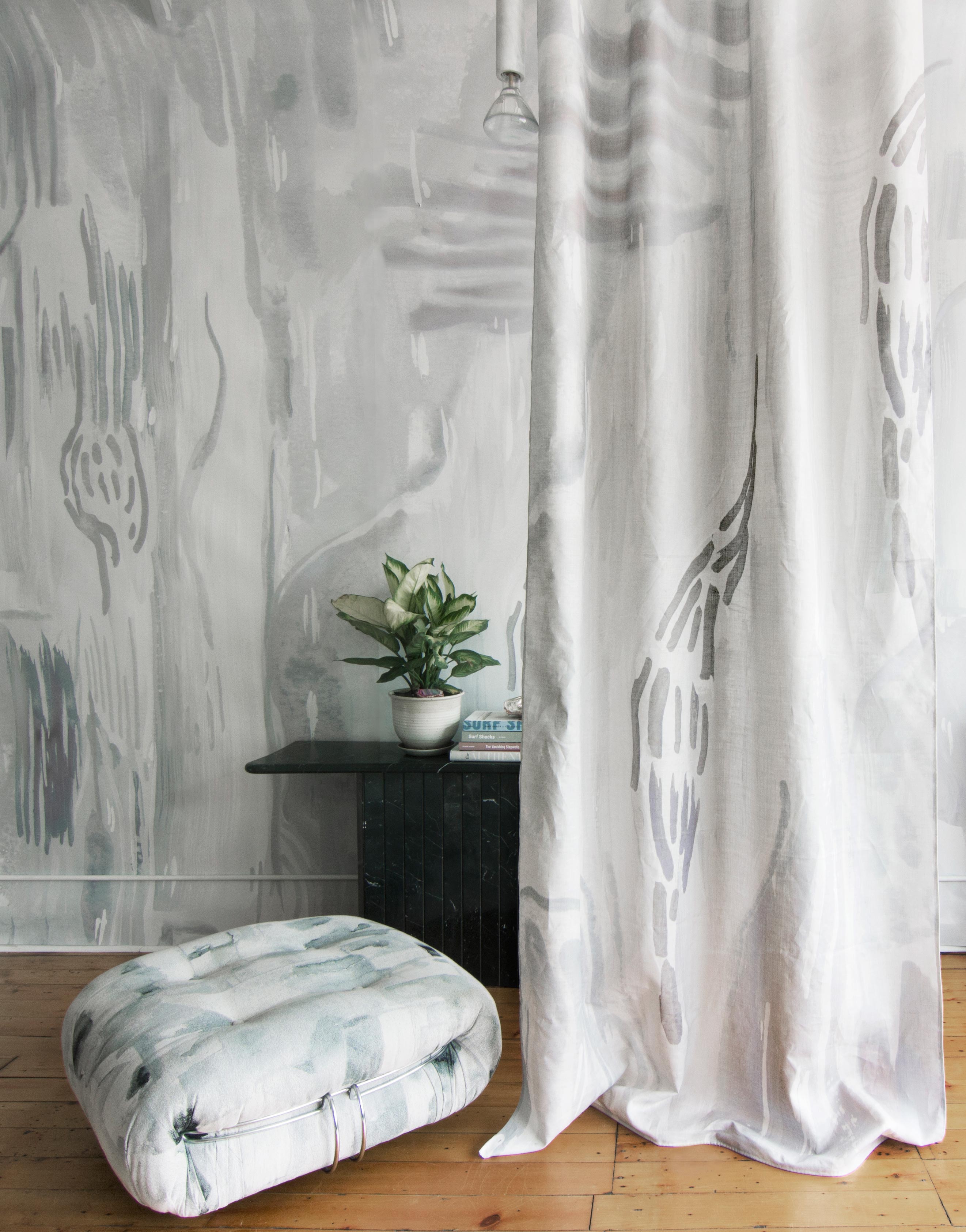 A floor pillow and curtain, both upholstered in coordinating watercolor paint prints in shades of gray and blue on white fields.