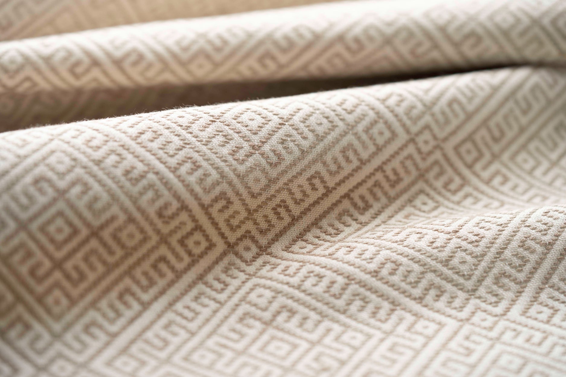 Close-up of textured beige fabric with geometric pattern lightly folded. 