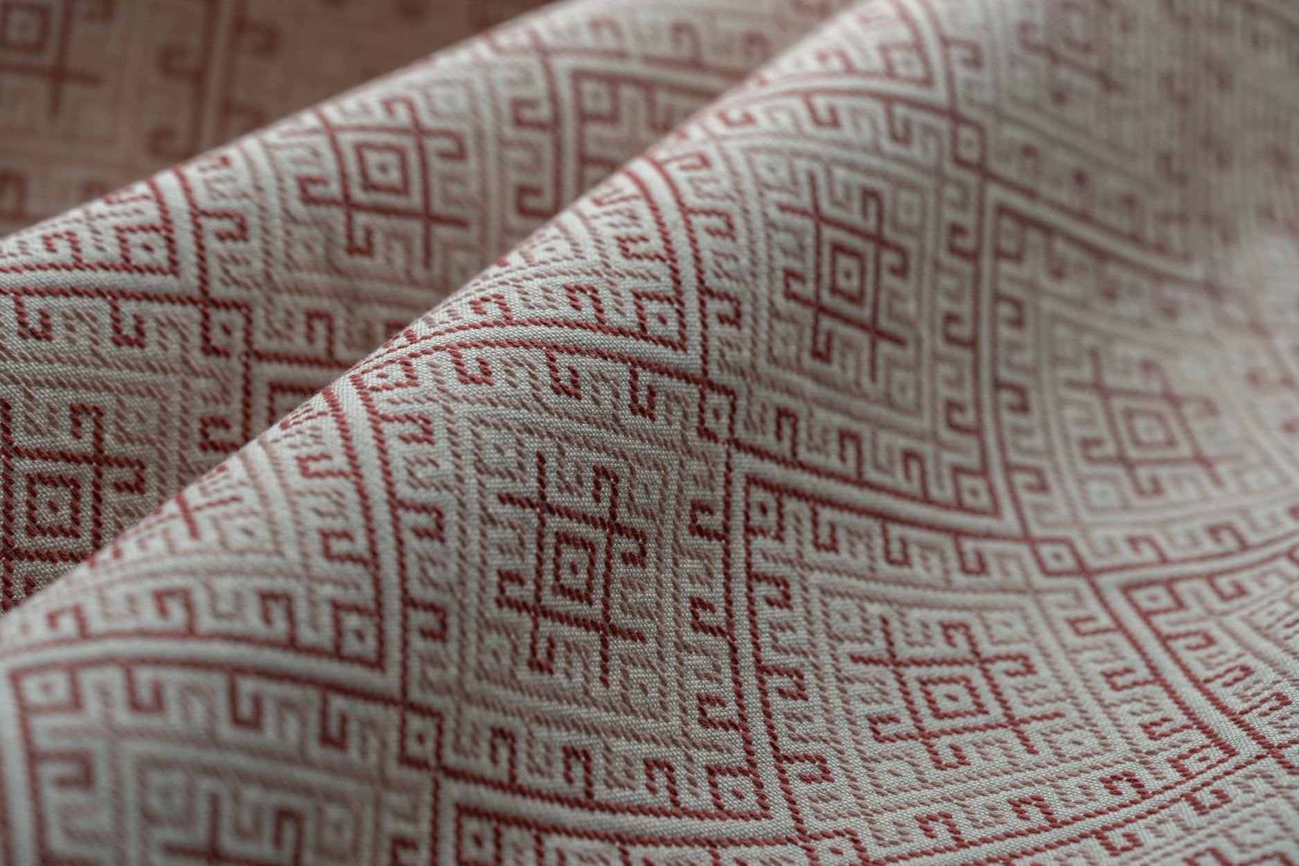 Close-up of fabric with a red geometric pattern on a beige background lightly folded