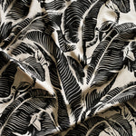 Close up of gently draped printed linen with bold high contrast tropical banana leaf pattern in black on cream.