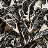 Close up of gently draped printed linen with bold high contrast tropical banana leaf pattern in black on cream.