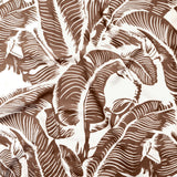 Close up of gently draped printed linen with bold high contrast tropical banana leaf pattern in dark brown on white. 