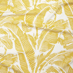 Close up of gently draped printed linen with bold high contrast tropical banana leaf pattern in yellow on white. 