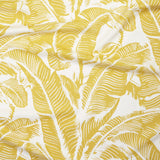 Close up of gently draped printed linen with bold high contrast tropical banana leaf pattern in yellow on white. 