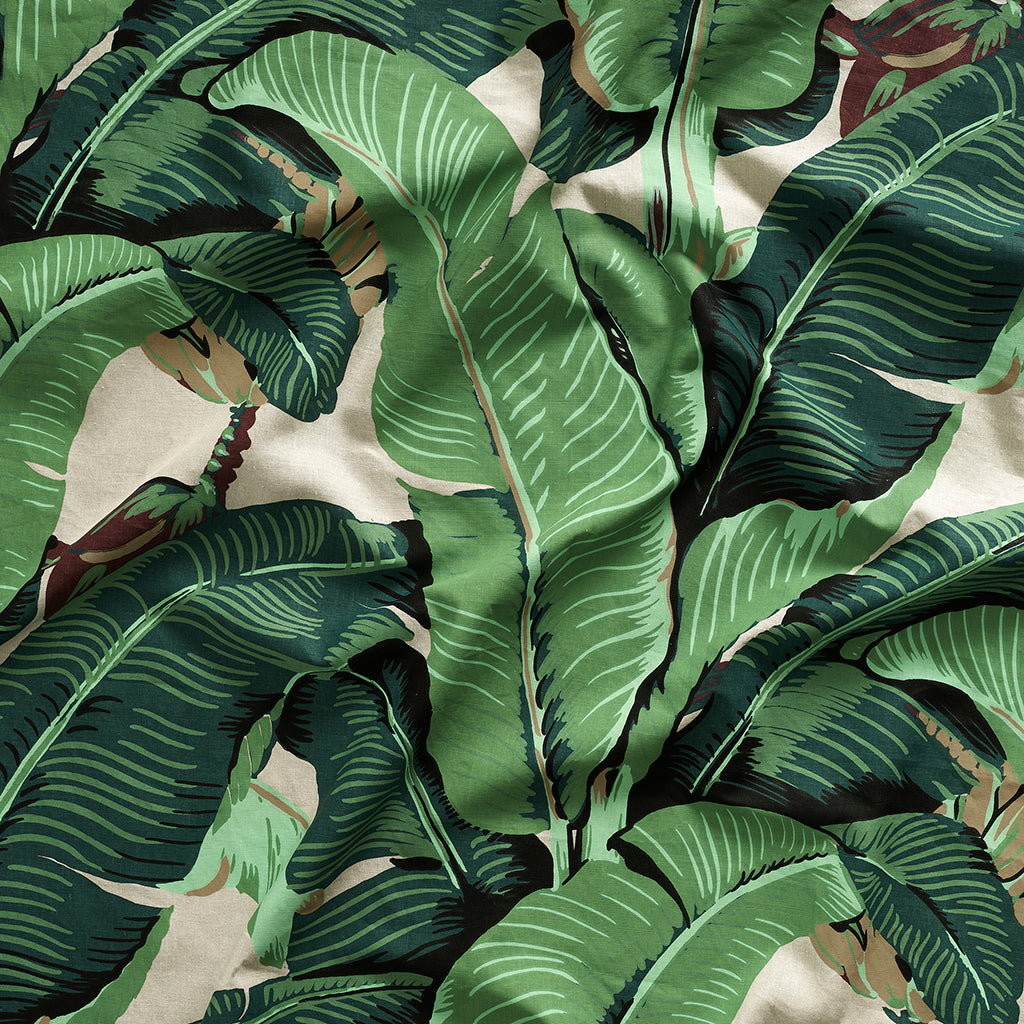Close up of gently draped printed linen with bold banana leaf in shades of green and brown on white.