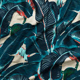 Close up of gently draped printed linen with bold banana leaf in shades of teal, navy and turquoise blue with green and coral accents on white.