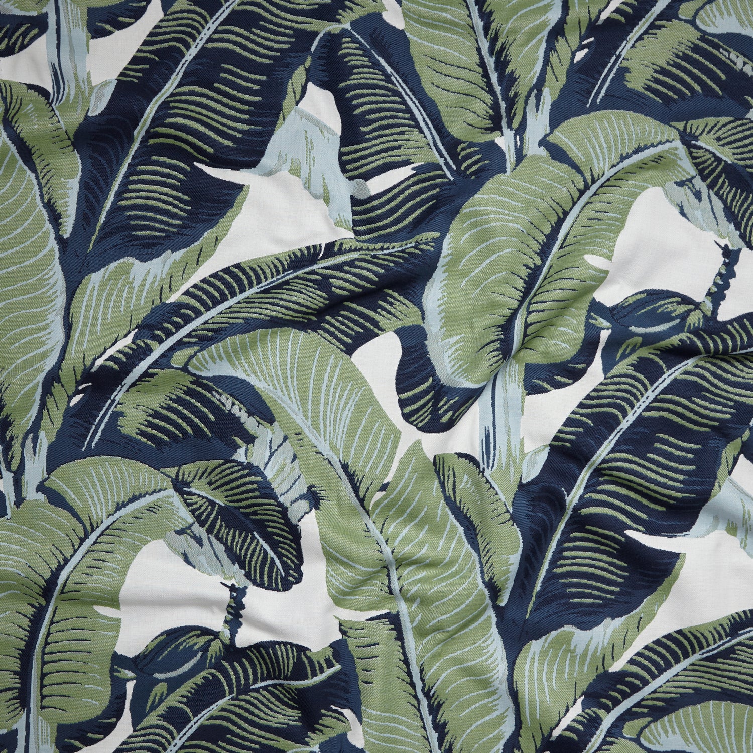 Close up of gently draped woven Indoor-Outdoor fabric with bold banana leaf in navy blue, green and light blue on cream.
