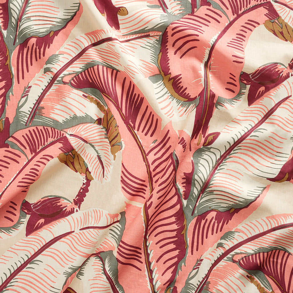 Close up of gently draped printed linen with bold banana leaf in shades of coral pink, magenta, grey and tan on cream,