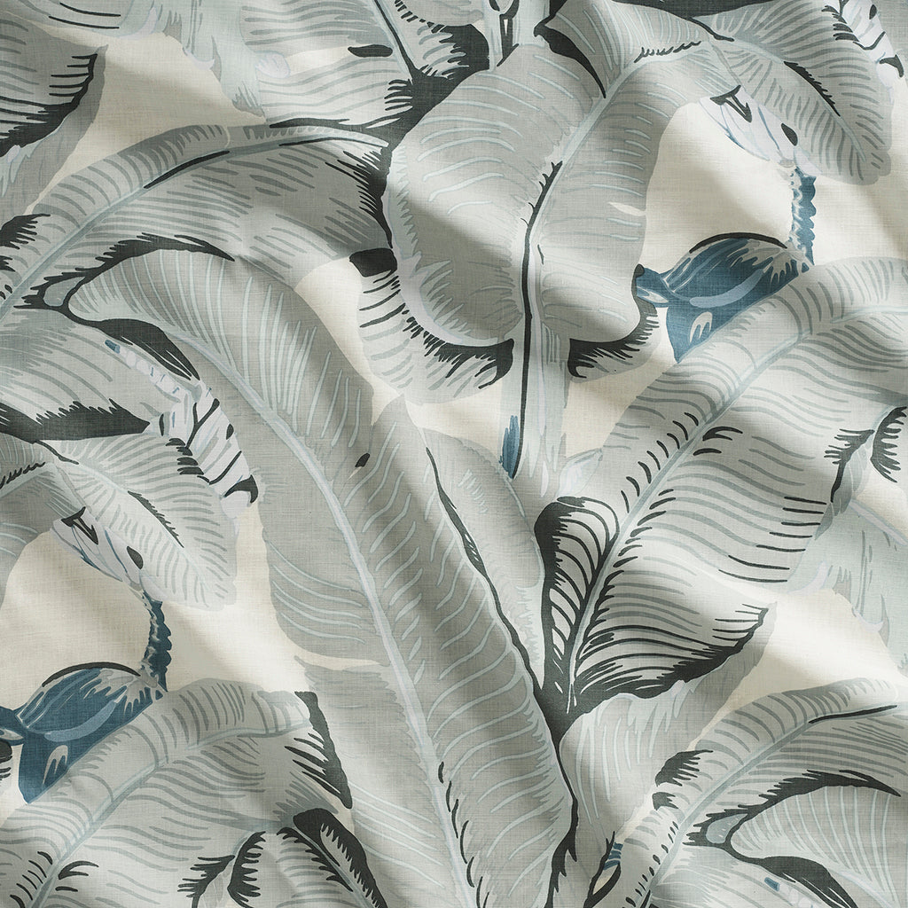 Close up of gently draped printed linen with bold banana leaf in shades of grey and steel blue on white.
