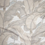 Close up of gently draped woven Indoor-Outdoor fabric with bold banana leaf in shades of beige on white.
