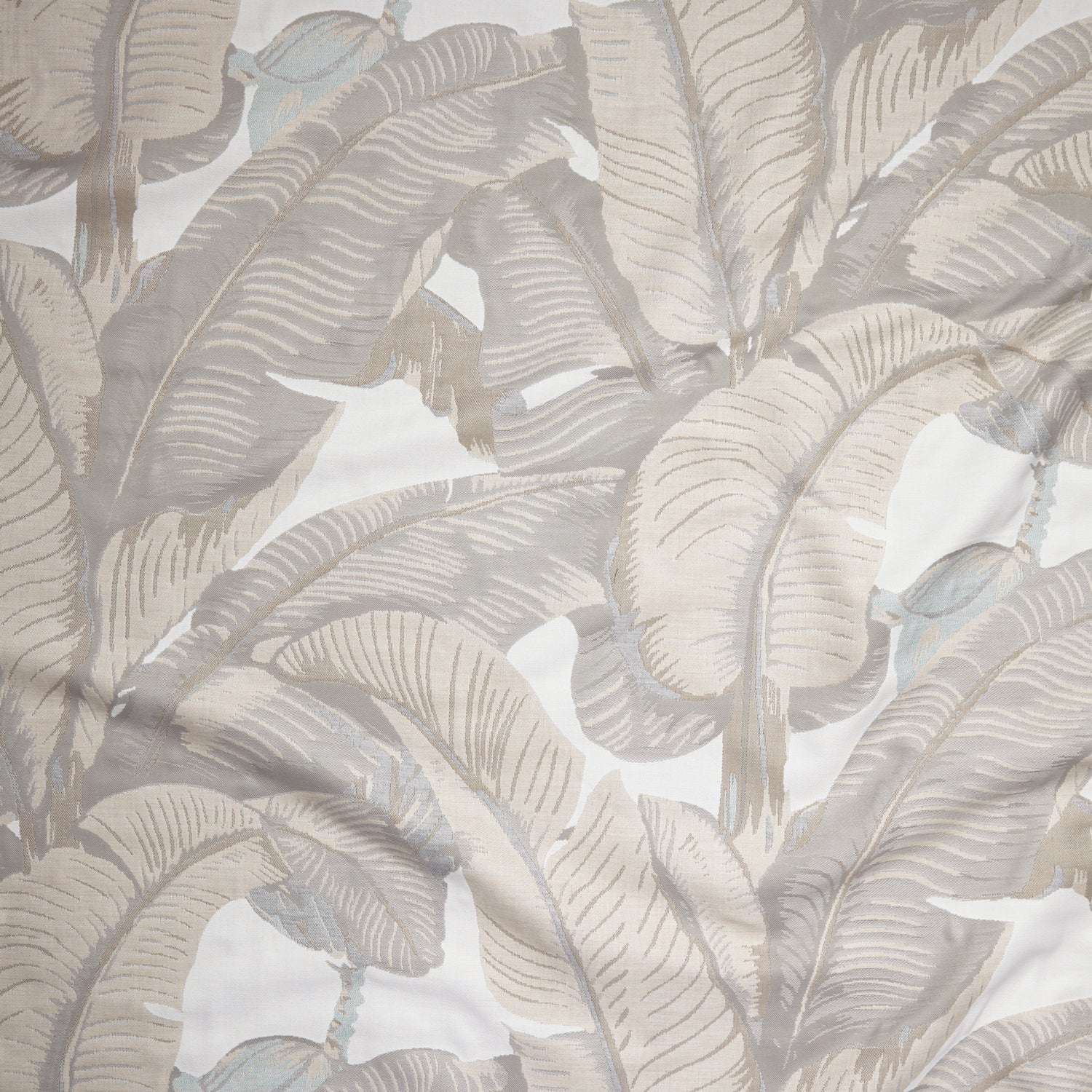 Close up of gently draped woven Indoor-Outdoor fabric with bold banana leaf in shades of beige on white.