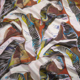 Close up of gently draped printed linen with linear painterly banana-leaf pattern in lilac, white, yellow, black and blue on a rust red and brown background. 