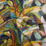 Close up of gently draped printed linen with a gestural painted banana leaf pattern in yellow, blue, green, white and orange on a navy blue field. 