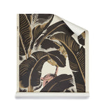A roll of banana leaf pattern wallpaper in dark brown, beige, and cream with a soft pink floral  accent. 