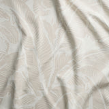 Close up of gently draped woven Indoor-Outdoor fabric with bold banana leaf pattern in white on beige.
