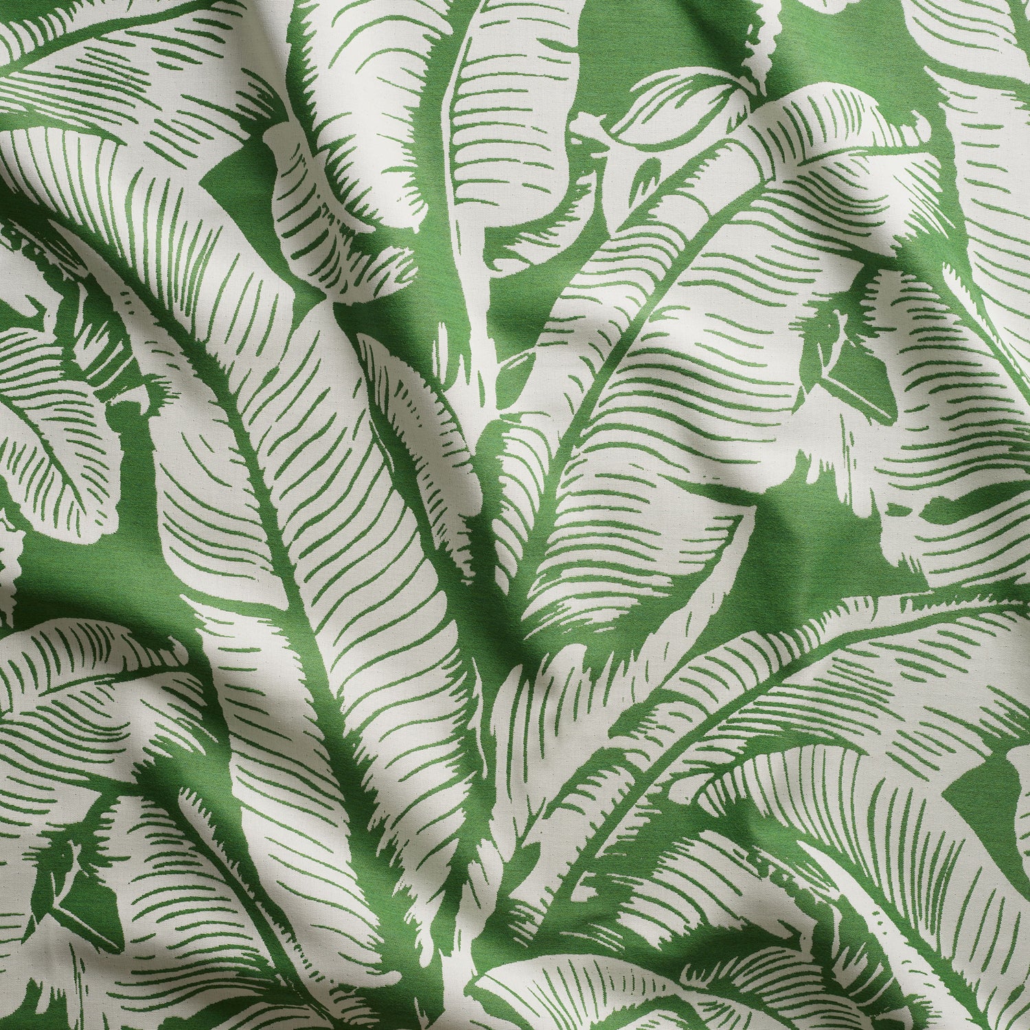 Close up of gently draped woven Indoor-Outdoor fabric with bold banana leaf pattern in white on grass green.