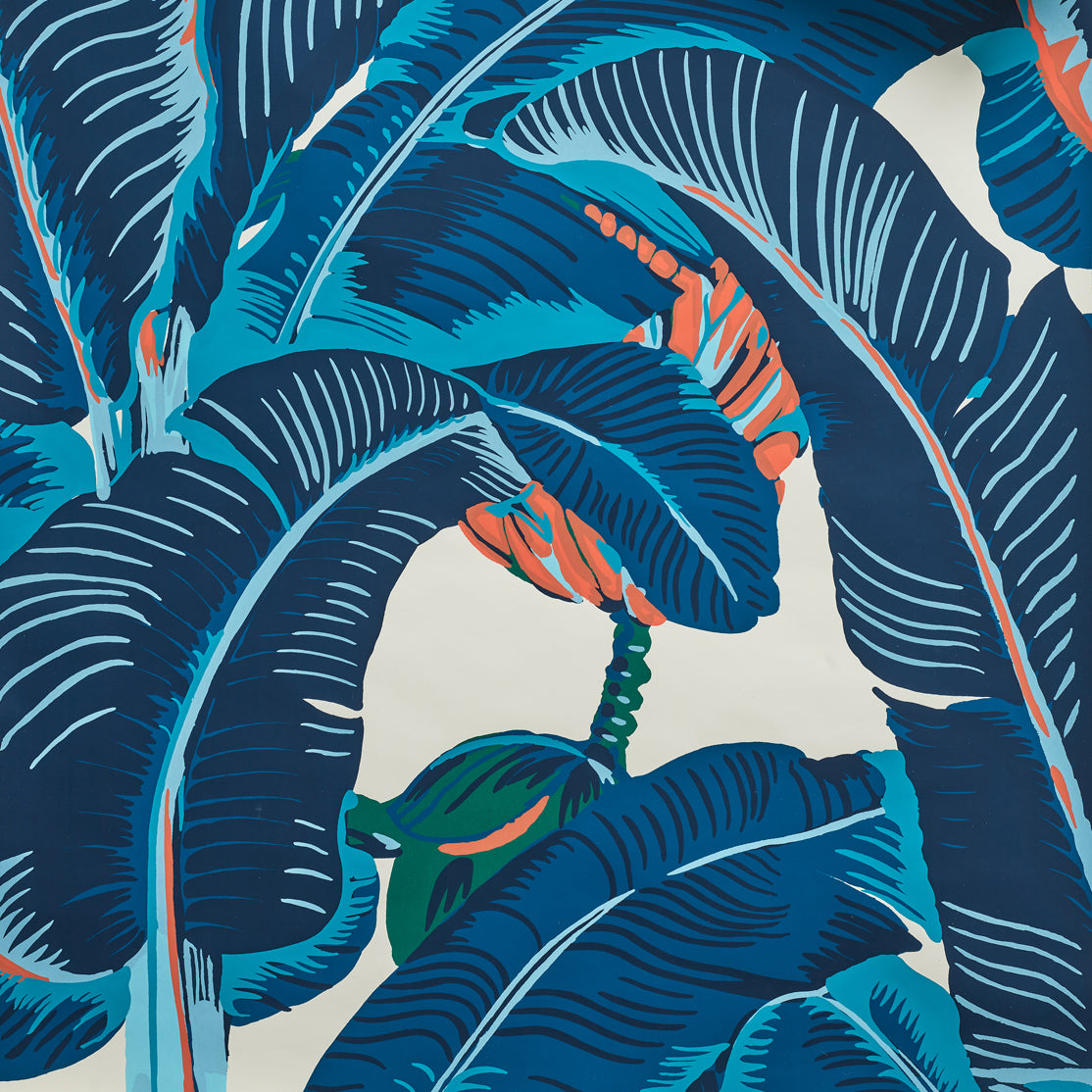 Close up of banana leaf pattern wallpaper featuring large tropical leaves in navy, teal and coral on an off-white background.