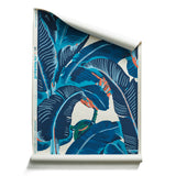 A roll of banana leaf pattern wallpaper featuring large tropical leaves in navy, teal and coral on an off-white background.