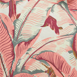 Close up of banana leaf pattern wallpaper featuring large tropical leaves in terracotta pink, cream, and muted gray-green tones on a light cream background.