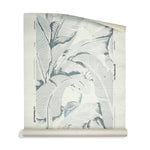 A roll of a tropical grassscloth wallpaper pattern featuring large, stylized palm leaves in shades of slate blue-gray and off-white.