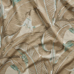 Close up of gently draped printed linen with bold banana leaf in shades of taupe and aqua blue on white.