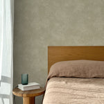 Bed with tan linens and wooden headboard, wooden side table  with white book and green glass, white floor length curtain against a white celestial dotted pattern on a sage green background. 