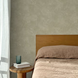 Bed with tan linens and wooden headboard, wooden side table  with white book and green glass, white floor length curtain against a white celestial dotted pattern on a sage green background. 