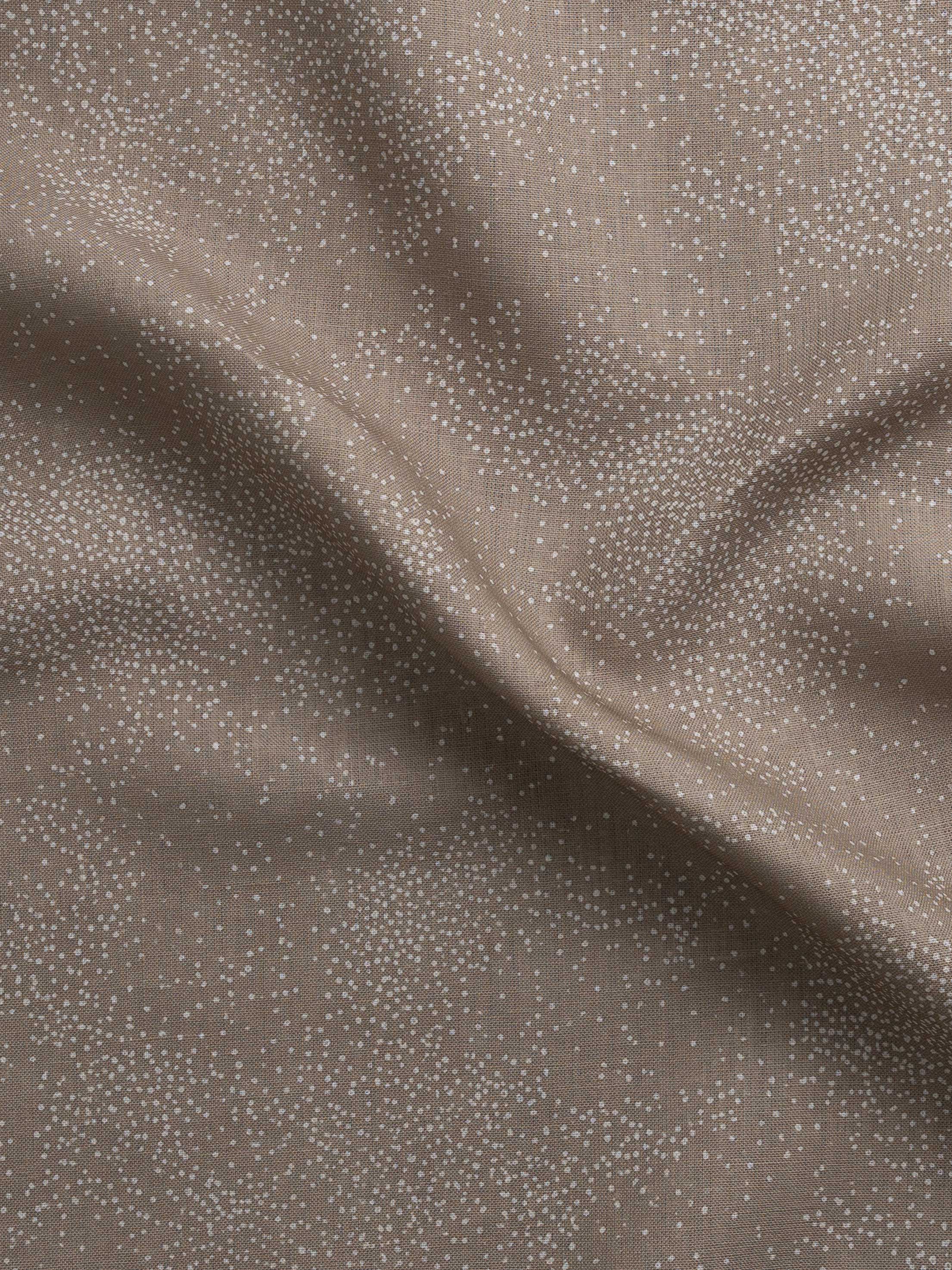 Detail of gently draped printed fabric with a white celestial dotted pattern on a warm beige background. 
