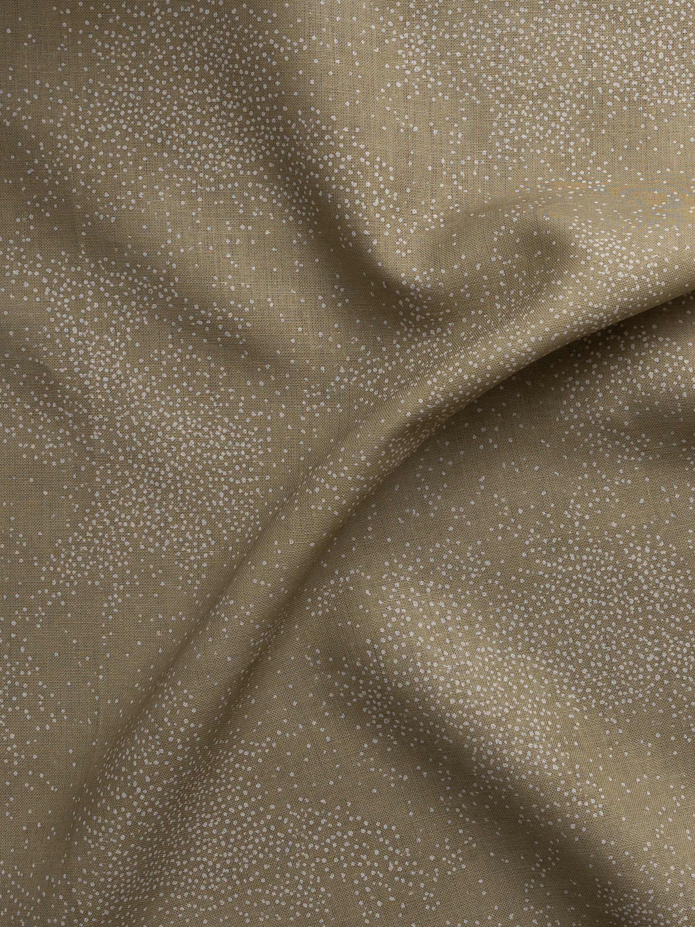 Detail of gently draped printed fabric with a white celestial dotted pattern on a soft tan background. 
