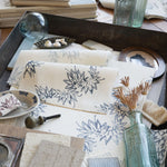 Desk setting with floral-patterned paper, inkwell, and bottles on a wooden surface.