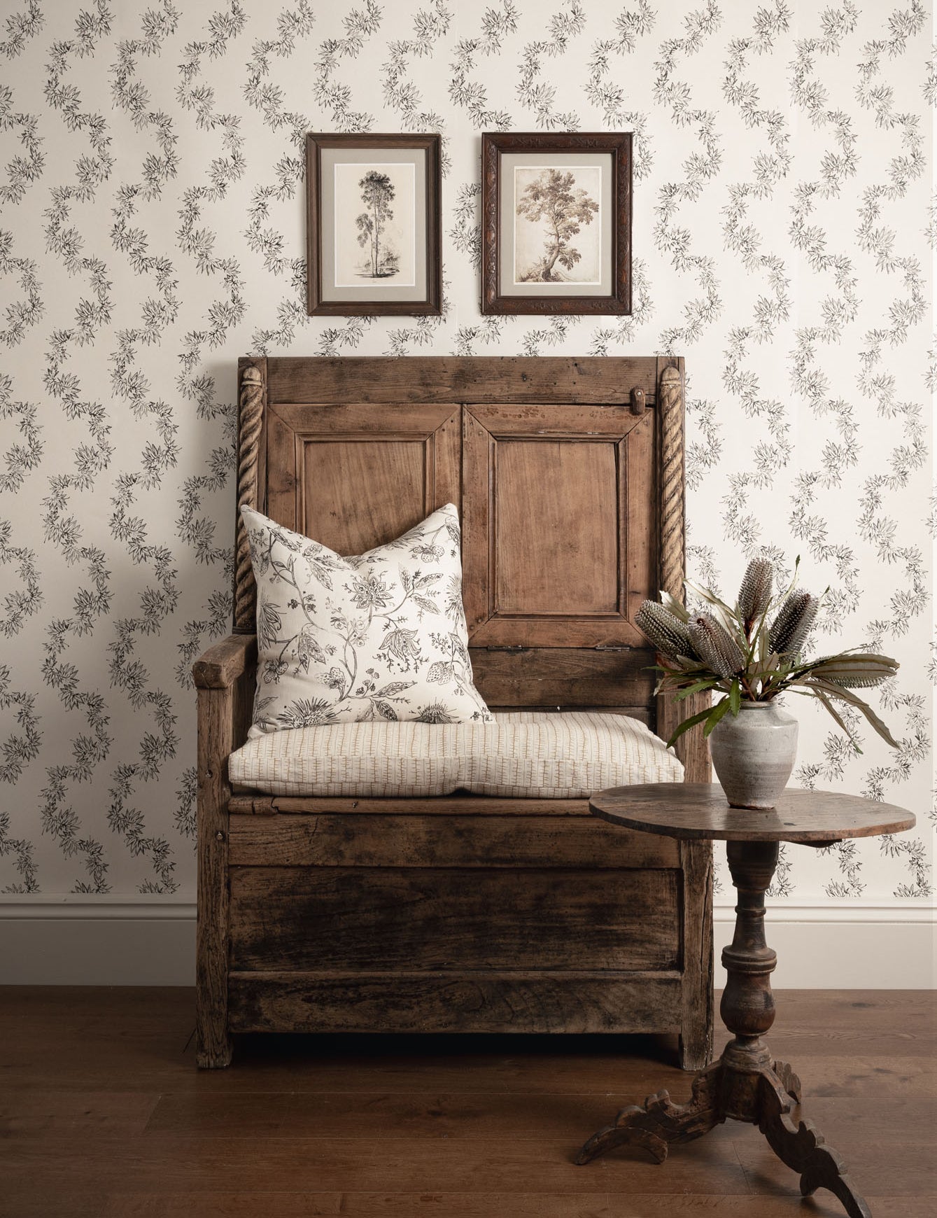 Wooden bench with floral cushion against a patterned wall with framed pictures.