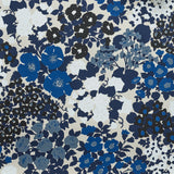 Close up of wallpaper with a dense flower and leaf pattern in shades of dark blue, grey, white and black on a beige background.