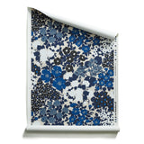 A roll of wallpaper with a dense flower and leaf pattern in shades of dark blue, grey, white and black on a beige background.