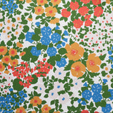 Close up of wallpaper with a dense flower and leaf pattern in shades of yellow, orange, blue, green and white. 