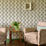 Living room scheme with orange and cream patterned chairs, sisal rug, rattan side table and a floral stripe wallpaper. 