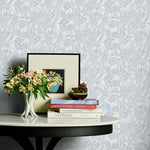 Decorative table with books and flowers against a patterned grey floral wallpaper.