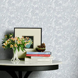 Decorative table with books and flowers against a patterned grey floral wallpaper.