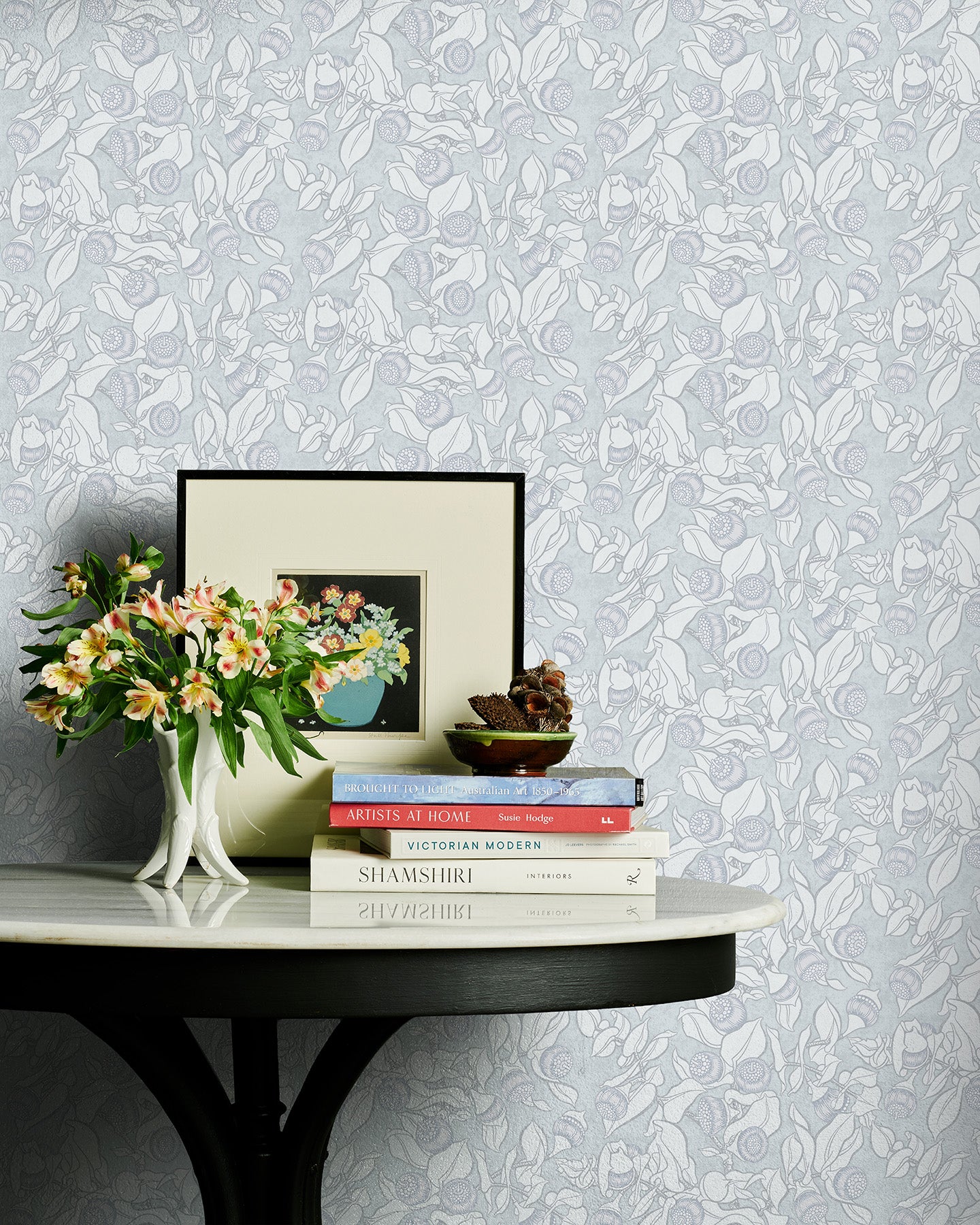 Decorative table with books and flowers against a patterned grey floral wallpaper.