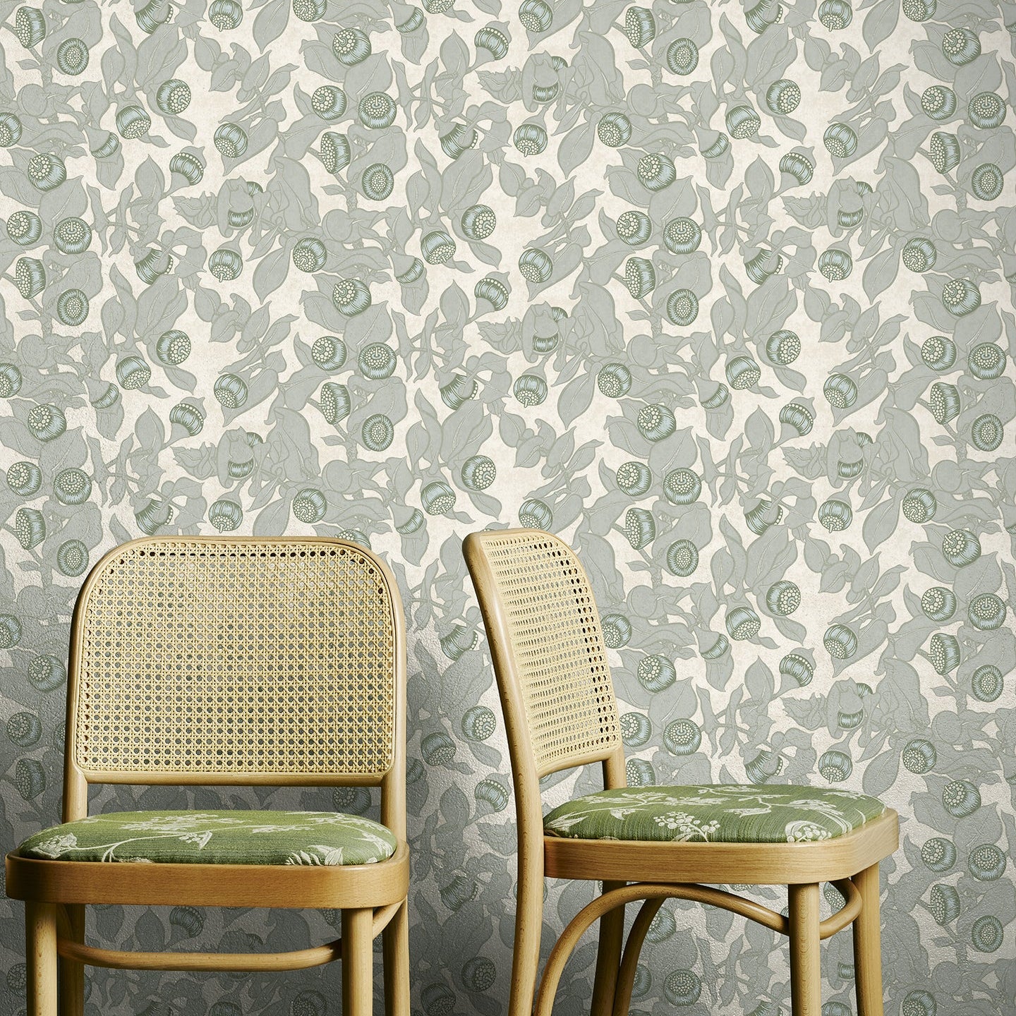 Two wooden chairs with green cushions against a floral-patterned wallpaper.