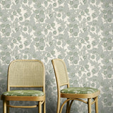 Two wooden chairs with green cushions against a floral-patterned wallpaper.