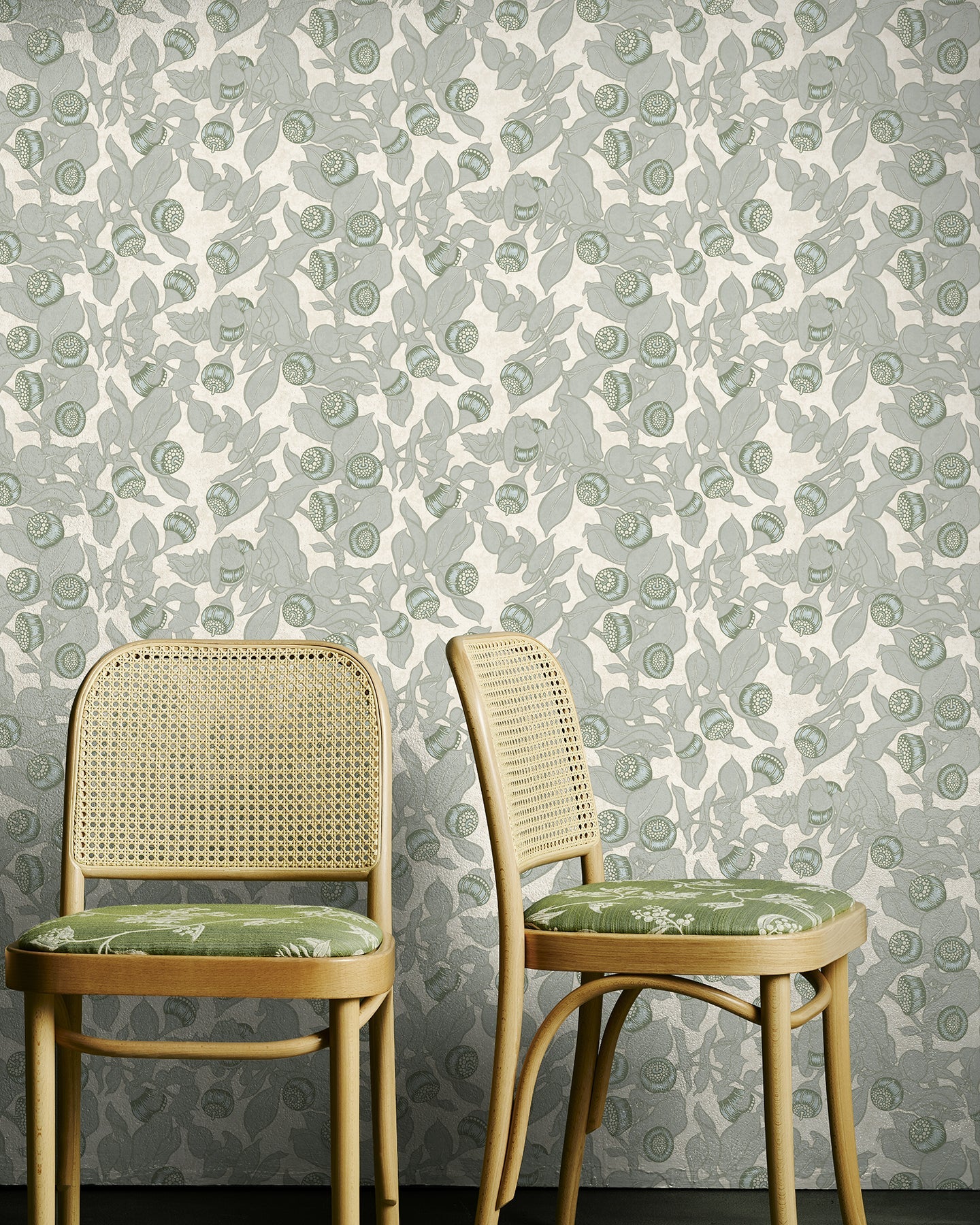 Two wooden chairs with green cushions against a floral-patterned wallpaper.