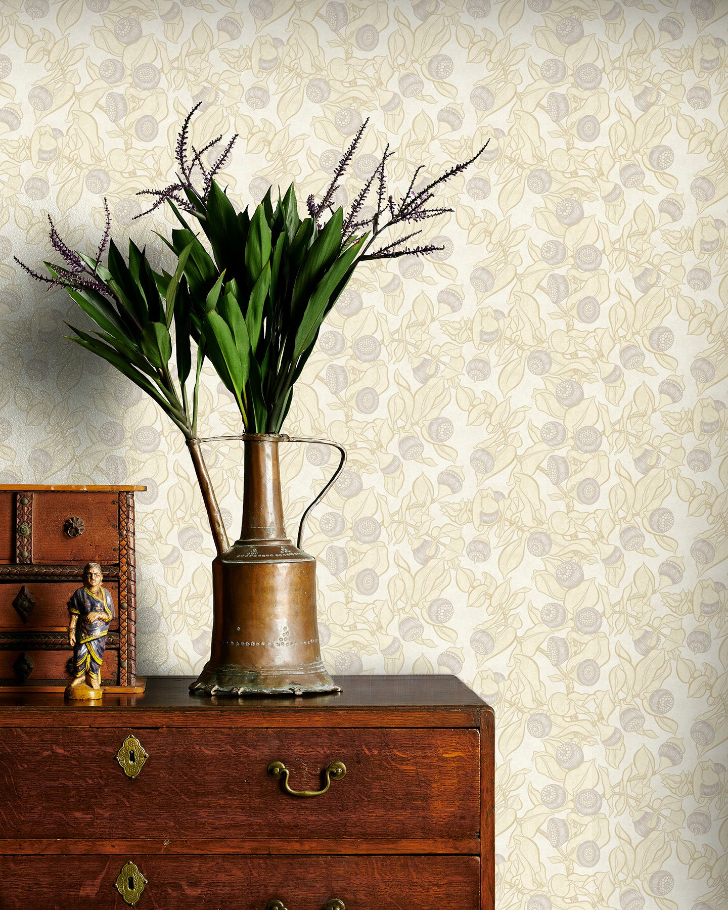 Decorative vase with plants on a wooden dresser against a soft yellow floral patterned wallpaper.